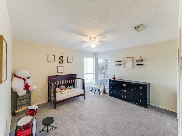 carpeted bedroom with a textured ceiling, a crib, and ceiling fan