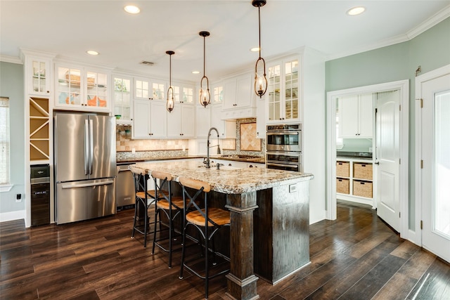 kitchen with appliances with stainless steel finishes, pendant lighting, white cabinetry, light stone countertops, and a center island with sink