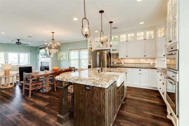 kitchen with sink, stainless steel refrigerator, white cabinetry, light stone countertops, and a center island with sink