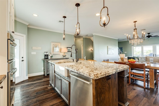 kitchen with sink, dark wood-type flooring, appliances with stainless steel finishes, hanging light fixtures, and a center island with sink