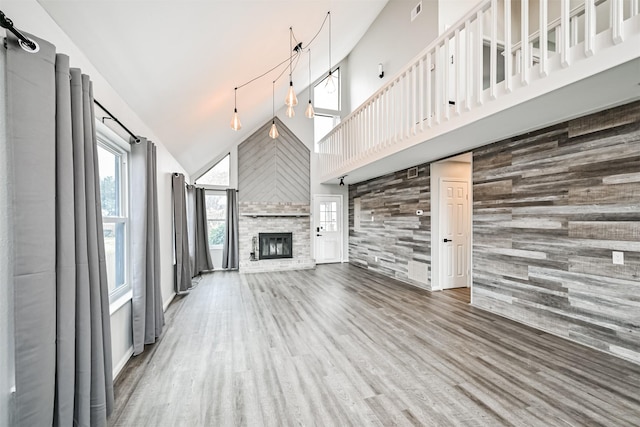 unfurnished living room featuring wood-type flooring, a fireplace, high vaulted ceiling, and wood walls