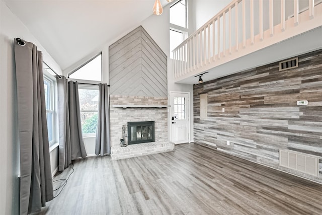 unfurnished living room with wood-type flooring, a fireplace, high vaulted ceiling, and wood walls