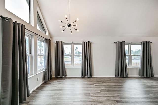 empty room featuring dark hardwood / wood-style floors, lofted ceiling, a healthy amount of sunlight, and an inviting chandelier