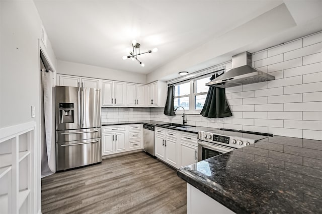 kitchen with appliances with stainless steel finishes, white cabinetry, sink, decorative backsplash, and wall chimney range hood