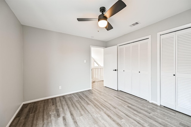 unfurnished bedroom featuring two closets, light hardwood / wood-style flooring, and ceiling fan