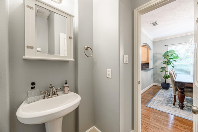 bathroom with hardwood / wood-style floors, ornamental molding, sink, and a textured ceiling