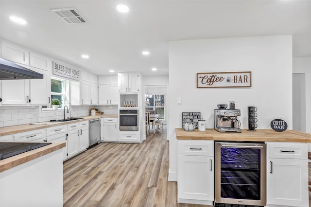 kitchen with white cabinetry, wooden counters, appliances with stainless steel finishes, beverage cooler, and backsplash