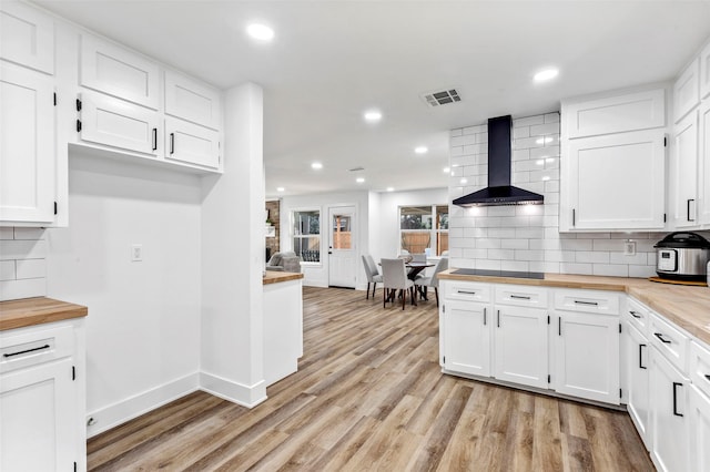 kitchen featuring wall chimney exhaust hood, butcher block counters, white cabinetry, light hardwood / wood-style flooring, and decorative backsplash