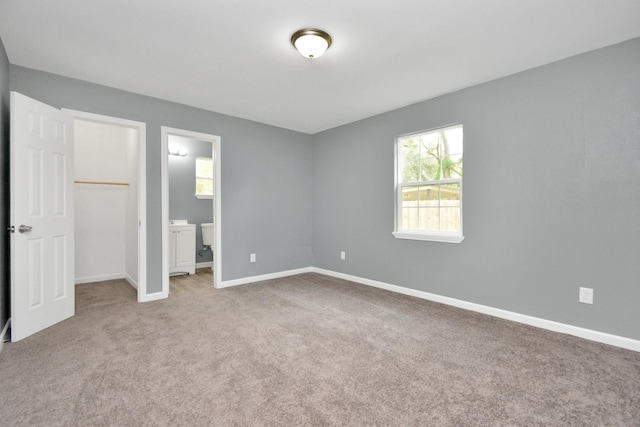 unfurnished bedroom featuring a walk in closet, ensuite bath, carpet floors, and a closet