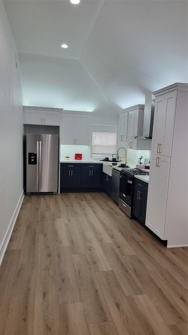 kitchen with lofted ceiling, stainless steel appliances, wall chimney exhaust hood, and white cabinets