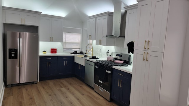 kitchen featuring appliances with stainless steel finishes, sink, white cabinets, backsplash, and wall chimney exhaust hood