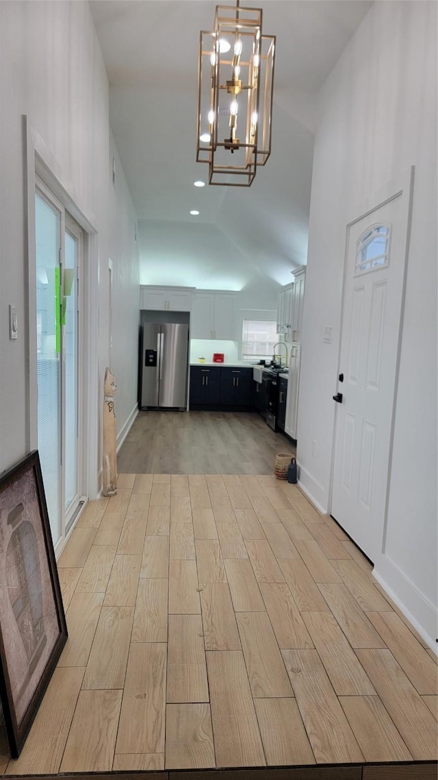 foyer featuring an inviting chandelier, vaulted ceiling, and light wood-type flooring