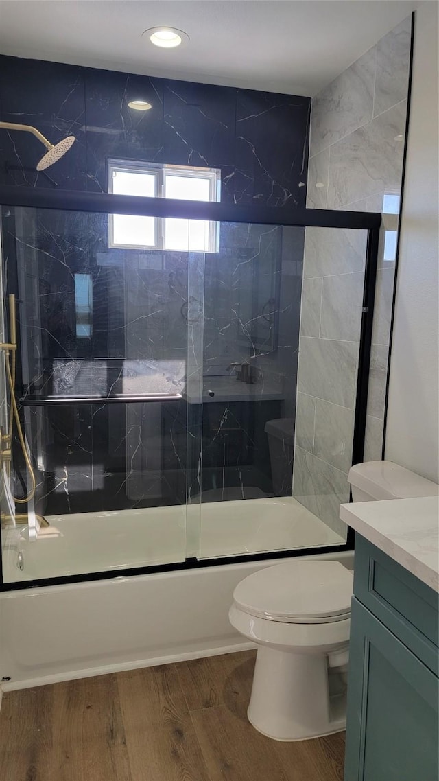 full bathroom with wood-type flooring, combined bath / shower with glass door, vanity, and toilet