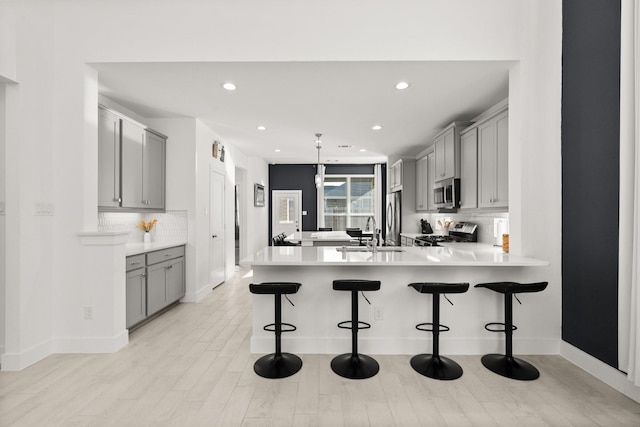 kitchen featuring decorative light fixtures, a breakfast bar area, backsplash, kitchen peninsula, and stainless steel appliances