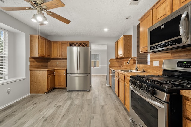 kitchen featuring appliances with stainless steel finishes, sink, decorative backsplash, light hardwood / wood-style floors, and a textured ceiling