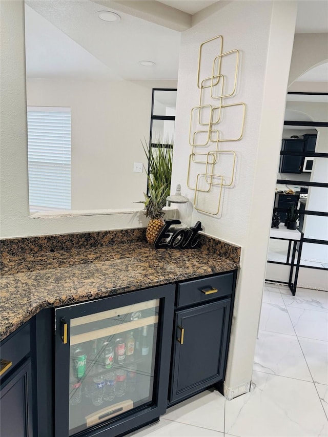 bar featuring dark stone countertops, blue cabinetry, and beverage cooler