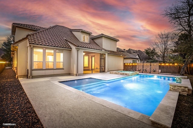 back house at dusk featuring a pool with hot tub and a patio area