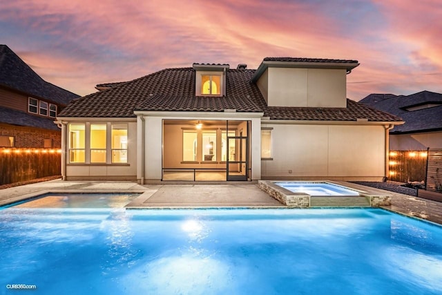 back house at dusk featuring a patio area and a pool with hot tub