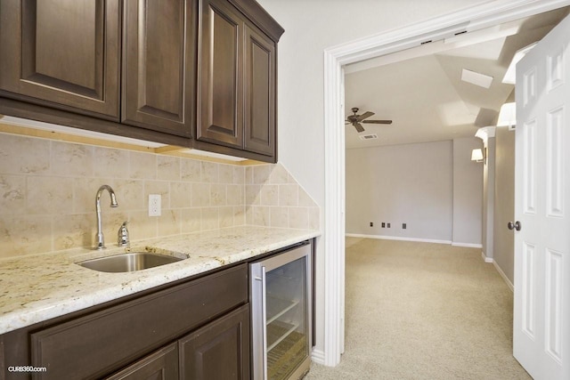 kitchen with dark brown cabinets, sink, light carpet, and beverage cooler