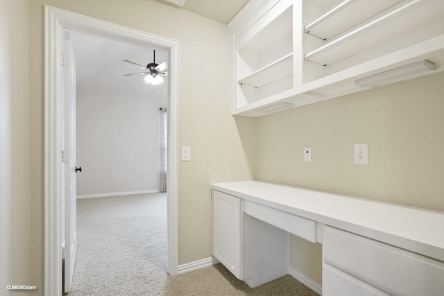 unfurnished office featuring light carpet, built in desk, and ceiling fan