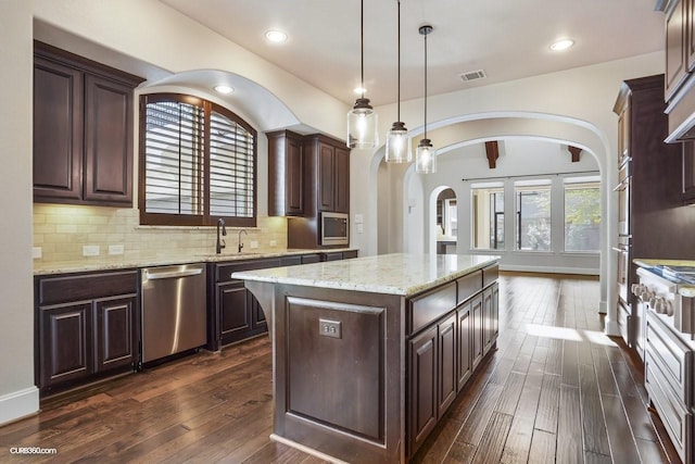 kitchen featuring a kitchen island, sink, hanging light fixtures, stainless steel dishwasher, and dark brown cabinetry