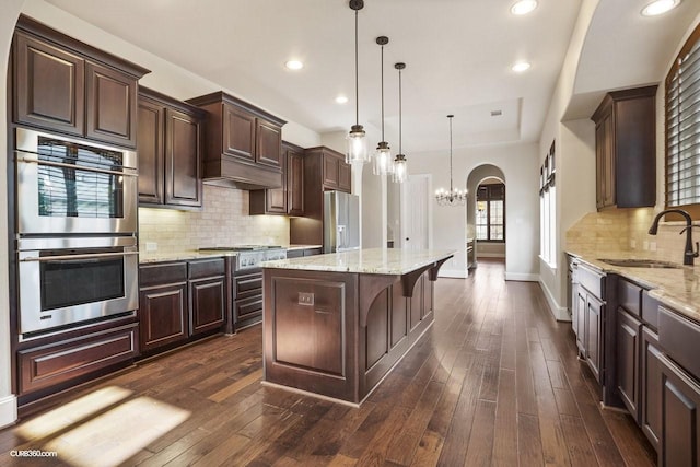 kitchen featuring pendant lighting, sink, appliances with stainless steel finishes, dark brown cabinetry, and a kitchen island