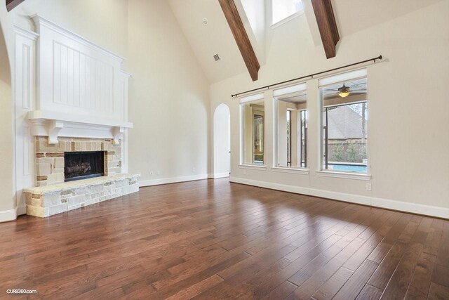 unfurnished living room featuring beam ceiling, a stone fireplace, dark wood-type flooring, and high vaulted ceiling