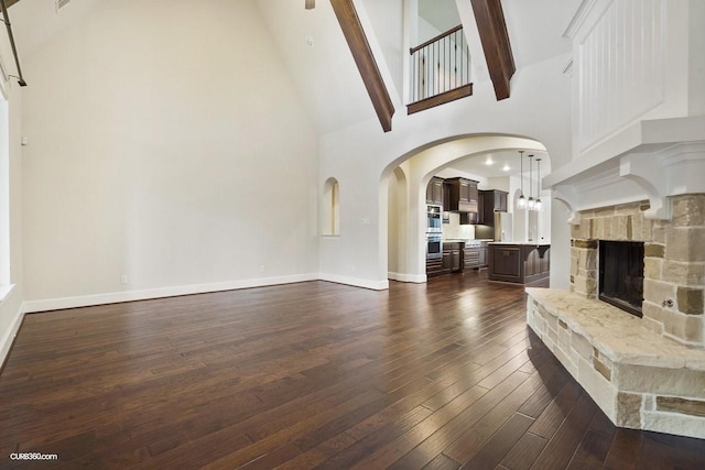 unfurnished living room featuring dark hardwood / wood-style flooring, a fireplace, high vaulted ceiling, and beamed ceiling