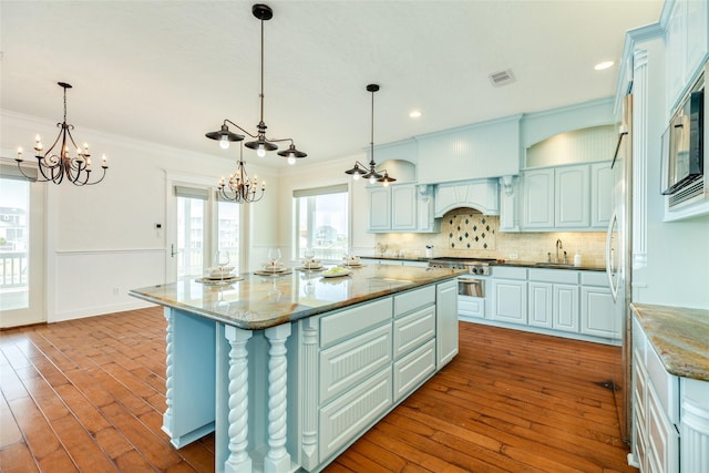 kitchen with hanging light fixtures, light stone countertops, a kitchen island, and ornamental molding