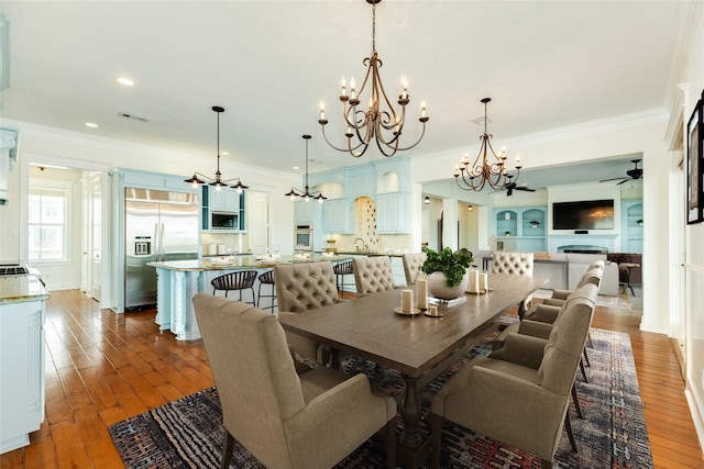 dining room featuring dark hardwood / wood-style flooring, sink, ceiling fan with notable chandelier, and ornamental molding