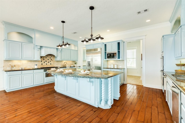 kitchen featuring pendant lighting, crown molding, dark stone countertops, a center island, and built in appliances