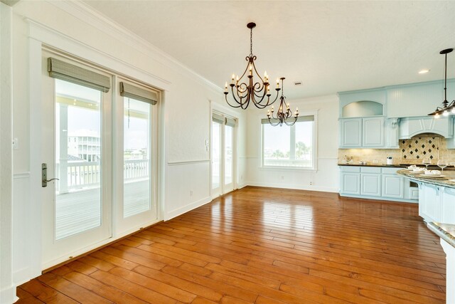 kitchen with crown molding, hanging light fixtures, light wood-type flooring, a notable chandelier, and backsplash