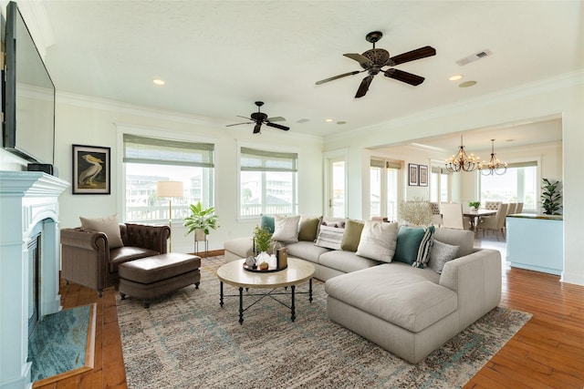 living room featuring ornamental molding, wood-type flooring, a premium fireplace, and ceiling fan with notable chandelier