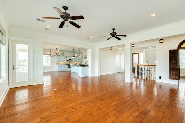 unfurnished living room featuring ornamental molding, ceiling fan with notable chandelier, and light wood-type flooring