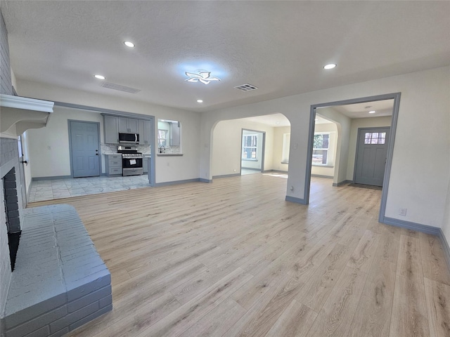 unfurnished living room featuring a brick fireplace, light hardwood / wood-style flooring, and a textured ceiling