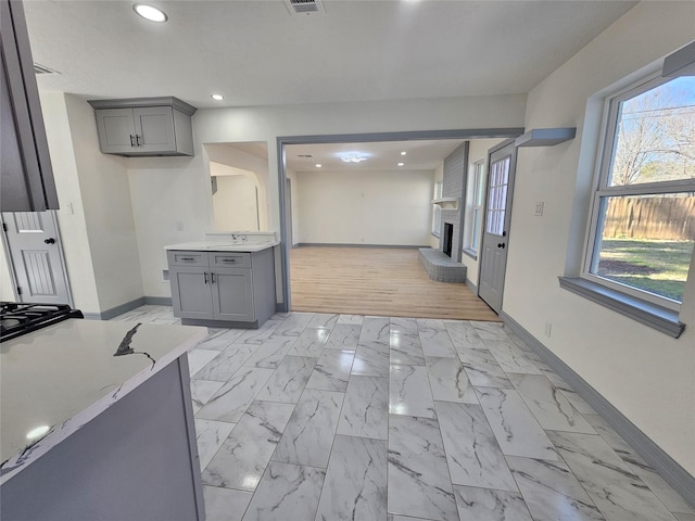 kitchen with gray cabinets, a healthy amount of sunlight, a large fireplace, and sink