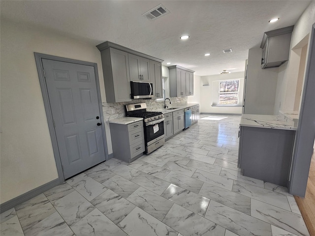 kitchen with sink, light stone counters, appliances with stainless steel finishes, gray cabinets, and decorative backsplash