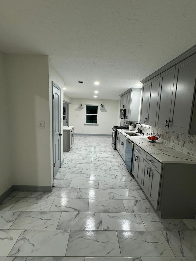 kitchen featuring stainless steel appliances, sink, gray cabinetry, and light stone counters