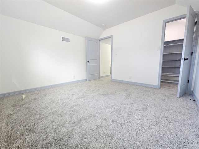 unfurnished bedroom featuring carpet flooring, lofted ceiling, a spacious closet, and a closet