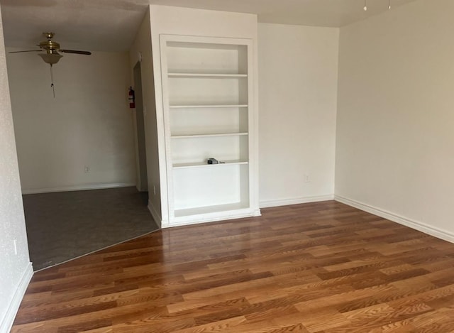 empty room with ceiling fan, dark hardwood / wood-style flooring, and built in features