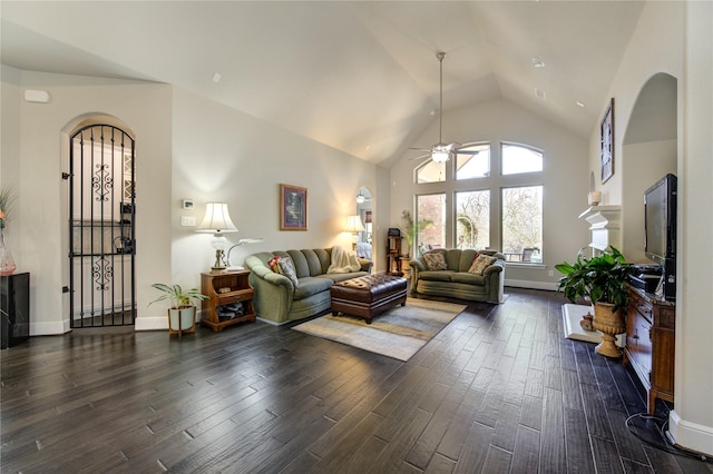 living room featuring arched walkways, dark wood-type flooring, ceiling fan, high vaulted ceiling, and baseboards