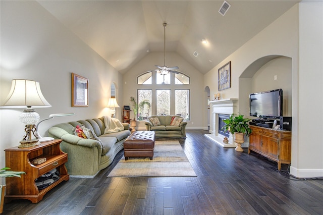 living area with high vaulted ceiling, dark wood finished floors, visible vents, baseboards, and a glass covered fireplace