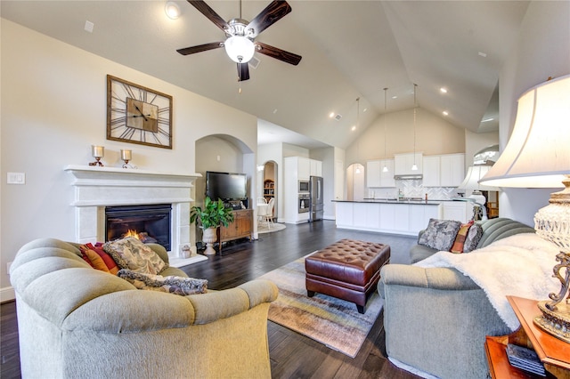 living area featuring arched walkways, ceiling fan, high vaulted ceiling, dark wood-style flooring, and a glass covered fireplace