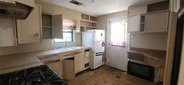 kitchen featuring sink, gas range, cream cabinetry, and white fridge