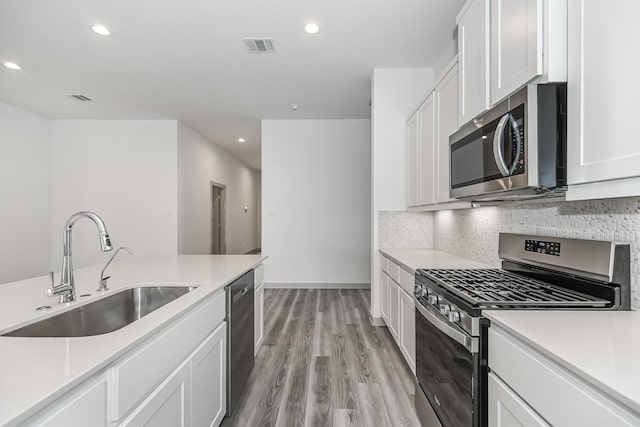 kitchen featuring sink, light hardwood / wood-style flooring, white cabinetry, stainless steel appliances, and tasteful backsplash