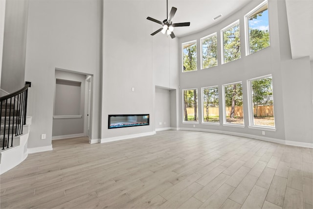 unfurnished living room featuring plenty of natural light, a towering ceiling, and light hardwood / wood-style floors