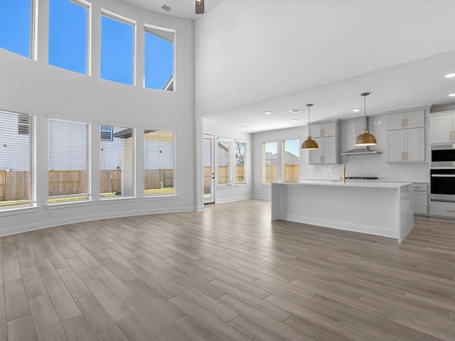 kitchen featuring stainless steel oven, decorative light fixtures, light wood-type flooring, an island with sink, and decorative backsplash