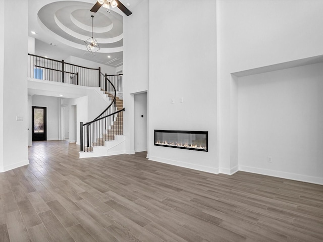 unfurnished living room with a raised ceiling, ceiling fan with notable chandelier, a towering ceiling, and hardwood / wood-style floors