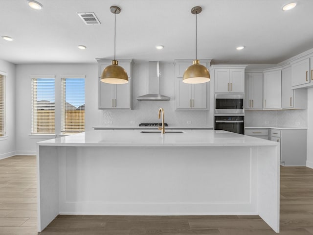 kitchen featuring a kitchen island with sink, decorative light fixtures, and wall chimney exhaust hood