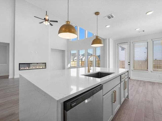 kitchen featuring pendant lighting, sink, light stone countertops, an island with sink, and stainless steel dishwasher